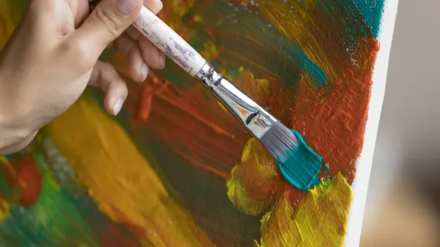 Closeup of person painting teal on a canvas
