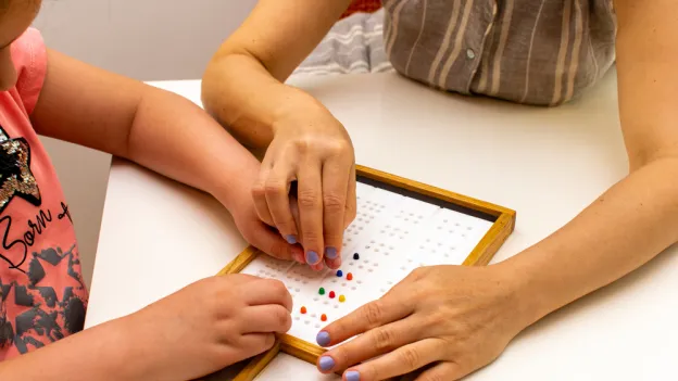 Teacher working with a student to learn braille alphabet