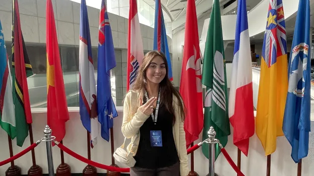 Kara Eaton gives the SFA "Axe 'em" hand sign in front of a row of country flags.
