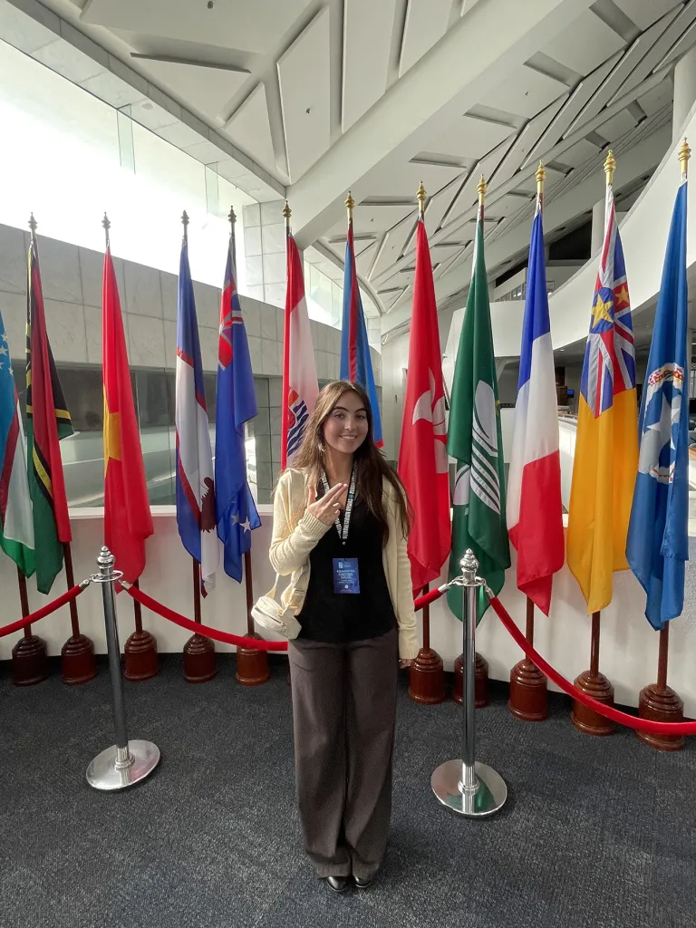 Kara Eaton gives the SFA "Axe 'em" hand sign in front of a row of country flags.