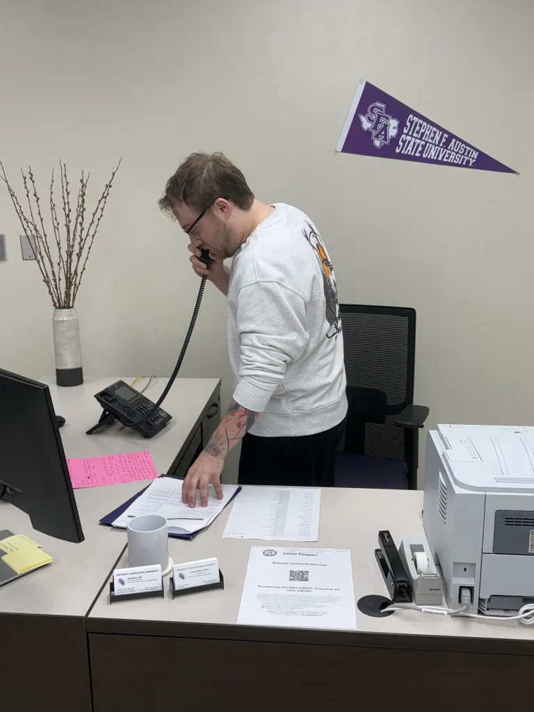 Kyle Sinopoli takes a sales phone call in an office with an SFA pennant in the background