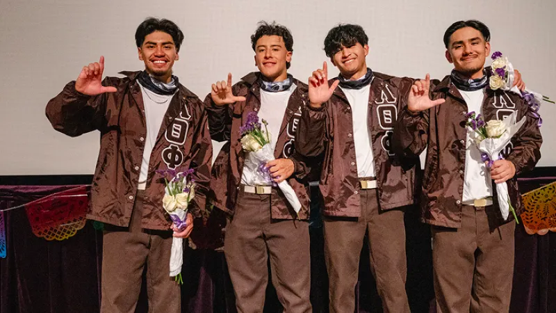 3 fraternity members in brown Alpha Theta Phi coats give hand signs