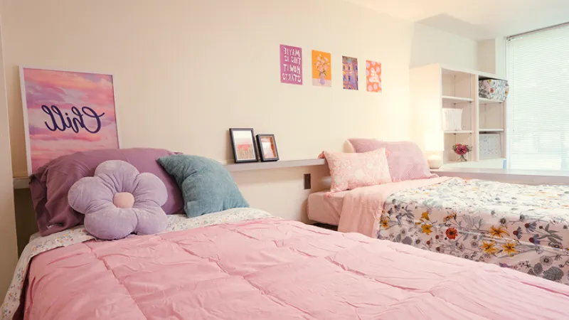Two double beds in a dorm room with floral and pink comforters and accessories