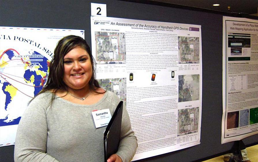 Student standing with a project on a wall behind her