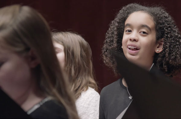 Child singing in a chorus looking at the camera and smiling