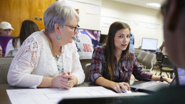 Several students and faculty member sit at a table and discuss a blueprint
