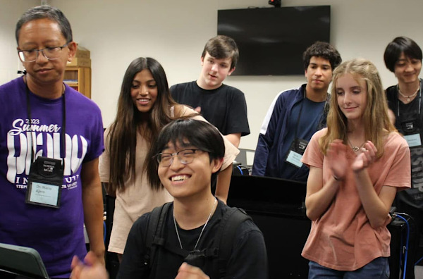 A group of students gather around a console piano to play a challenge game