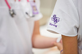 two nursing students with closeup of SFA nursing logo