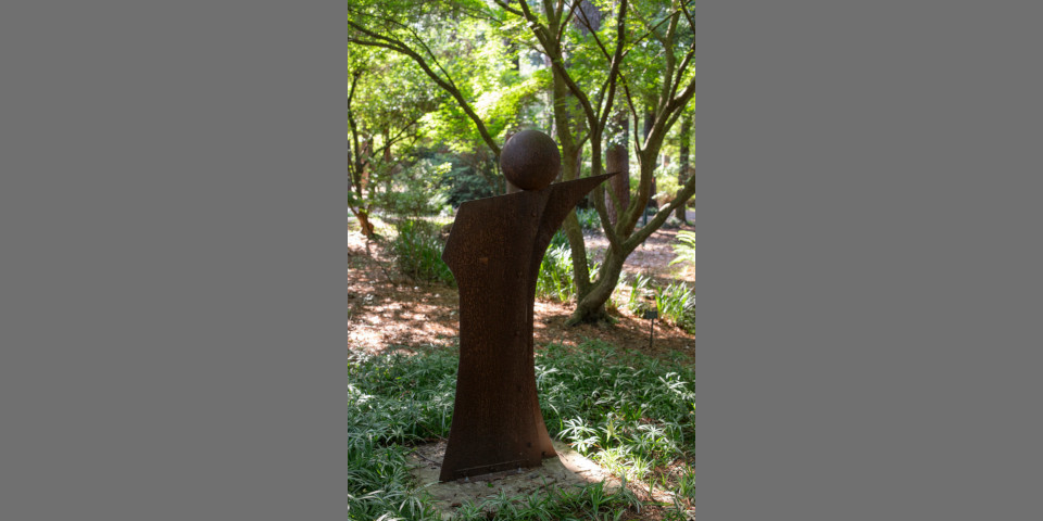 A metal sculpture of an orb balanced on an angled plane in the SFA Gardens