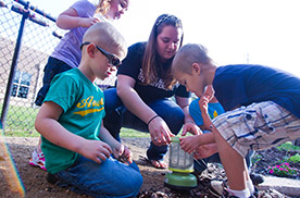 adult helping children plant a garden