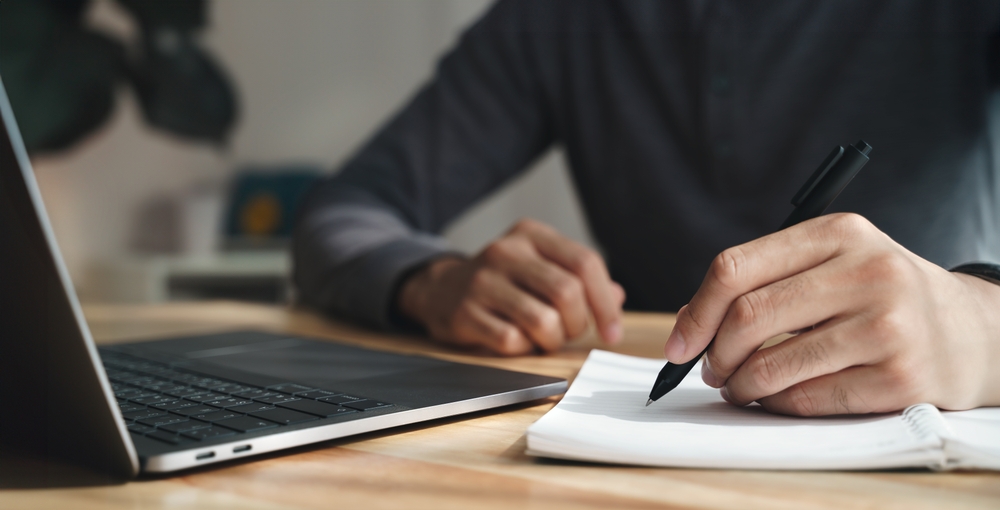 Closeup of person taking notes at a laptop