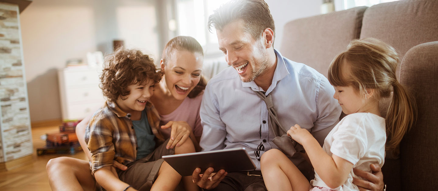 family of four looking at iPad together and laughing