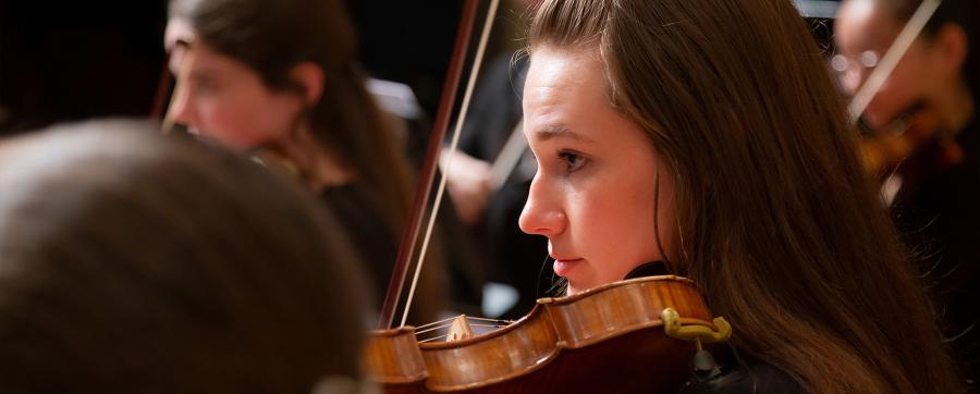 A closeup view of a violin student performing during an orchestra concert
