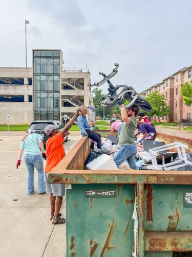 Two volunteers assist each other in handing off a chair in good condition from a collection bin