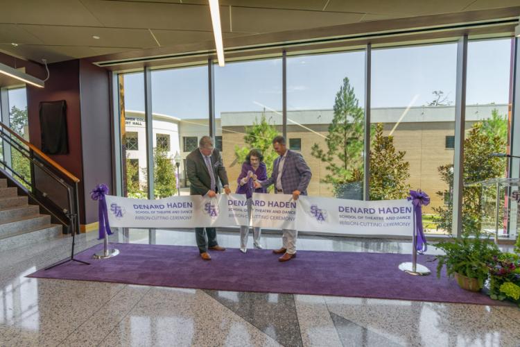 Standing on a purple carpet with a windowed backdrop of trees, Priscilla “Prissy” Abshier Sliva is assisted by Dr. Gary Wurtz and Dr. Neal Weaver in cutting a ceremonial ribbon.