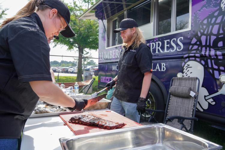 Axes and Embers team members prepare barbecue on a table next to the Lumberjack Express mobile food lab
