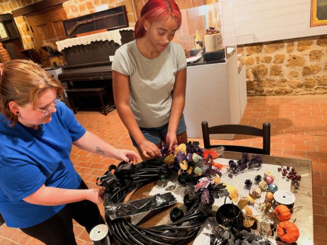 Two SFA student workers prepare a black Halloween wreath with various Halloween-themed decorations